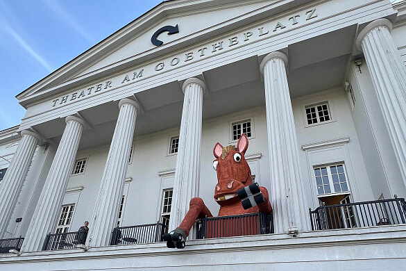 großer Pferdekopf mit zwei Beinen aus Pappmachè auf dem Balkon des Theaters Bremen, links steht ein Mensch, der deutlich kleiner als das Kunstwerk ist